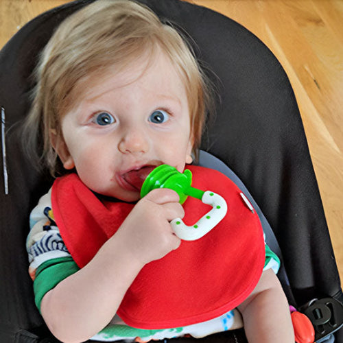 grignoteuse bebe vert et blanc dans la bouche de bébé assis dans sa chaise haute