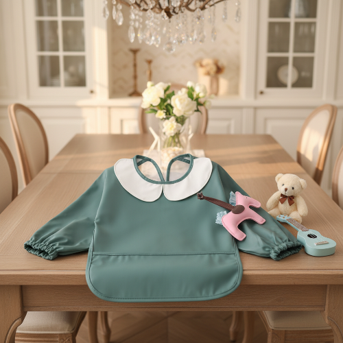 Bavoir imperméable bébé vert et le collet blanc sur la table de cuisine avec ourson en peluche et petite guitard