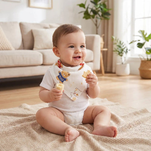 Bavoir bandana au cou de bébé qui mange une collation assis sur une couverture entrain de manger une banane