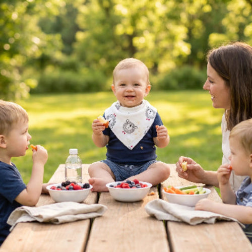 Bavoir bandana coton au cou de bébé assis sur une couverture au parc avec maman entrain de manger des collation