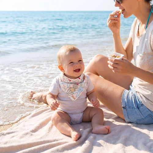Bavoir bandana au cou de bébé avec maman qui lui donne une collation sur le bord de la mer