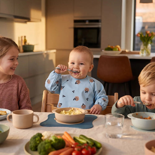 Bavoir imnperméable au cou de bébé entrain de manger à la table de cuisine avec son sa soeur et son frère