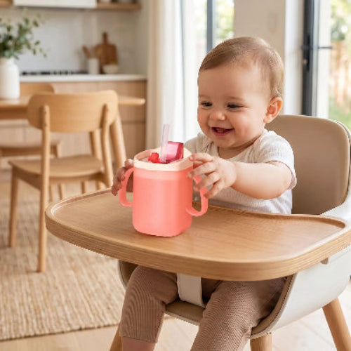 Tasse pour bébé évolutive rose sur la chaise haute avec bébé